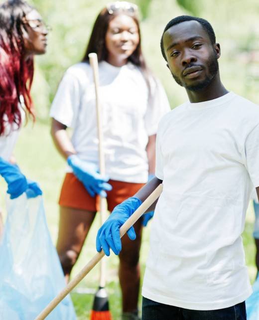 Group of happy african volunteers with garbage bags cleaning area in park. Africa volunteering, charity, people and ecology concept.