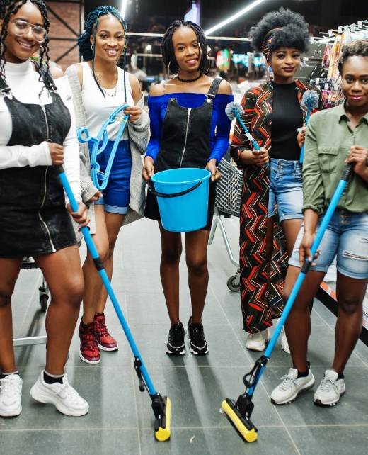 Group of five african womans with dust mop, toilet brush and bucket having fun in household cleaning items department in supermarket.