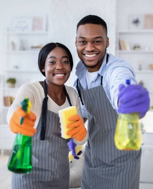 Happy black guy and his wife aiming spray detergents at camera, performing domestic cleanup, indoors. Millennial African American couple keeping their home tidy and clean